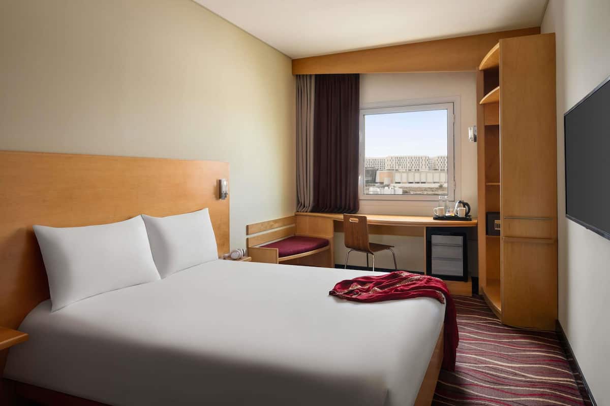 A hotel room with a bed, desk, chair, and a view through the window.