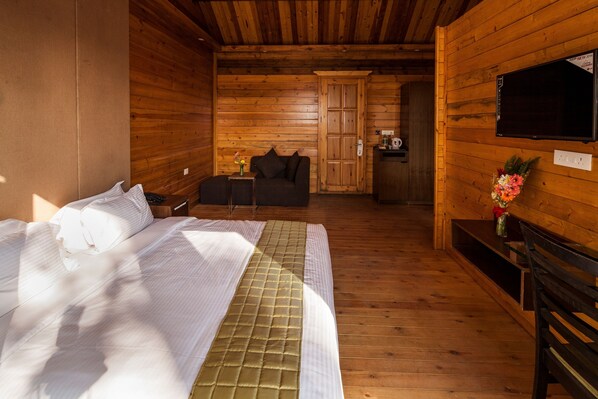 A wooden cabin room with a bed, a sofa, a TV, and a small table with a vase of flowers.