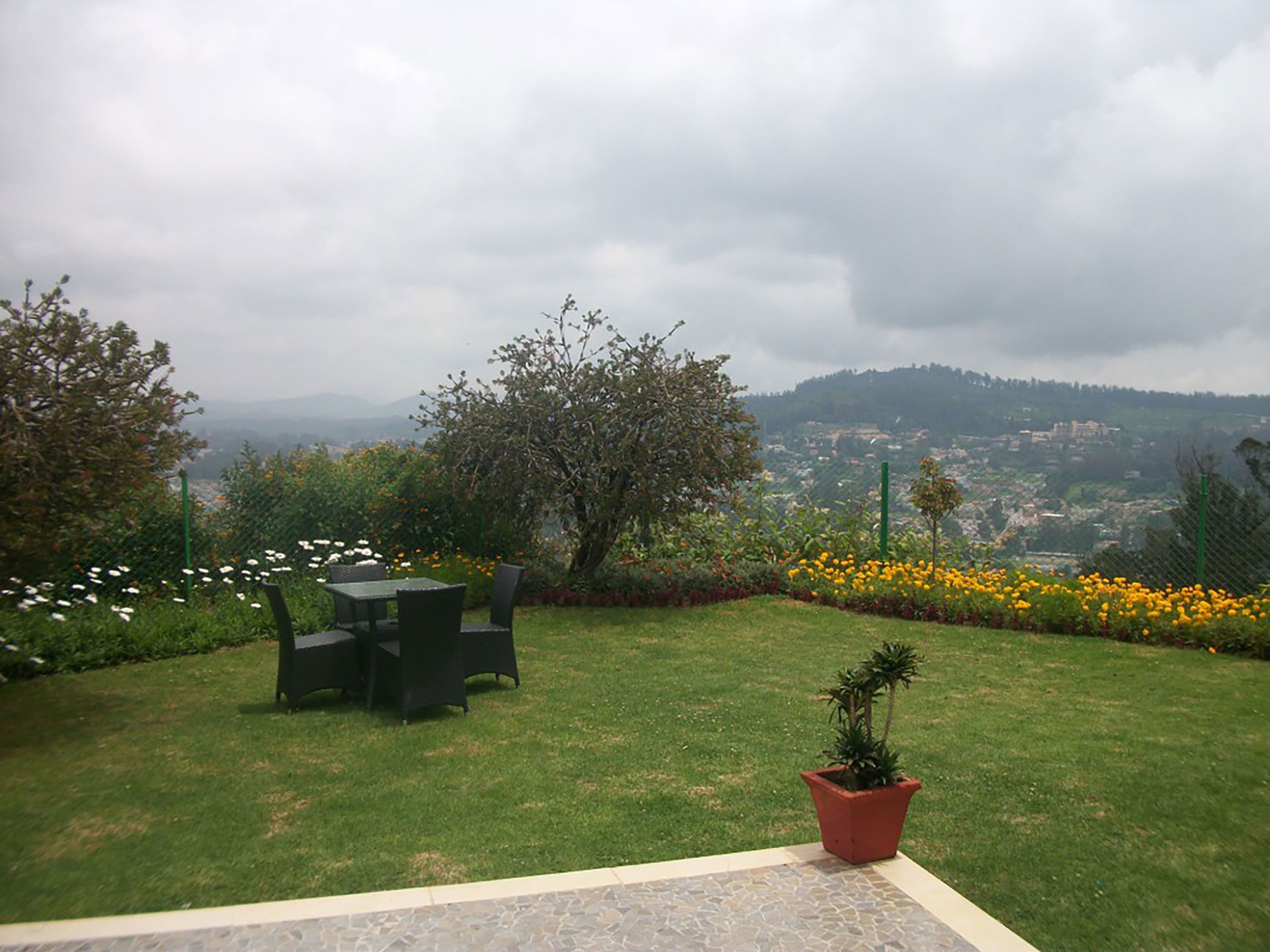 Un jardín con una mesa y sillas, una planta en maceta y vistas de un valle con casas.