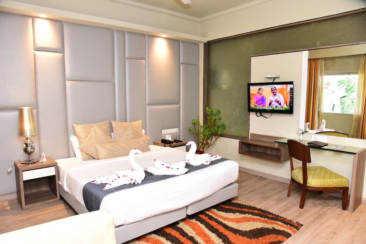 Una habitación de hotel con cama, escritorio, silla, televisor y una planta en maceta.