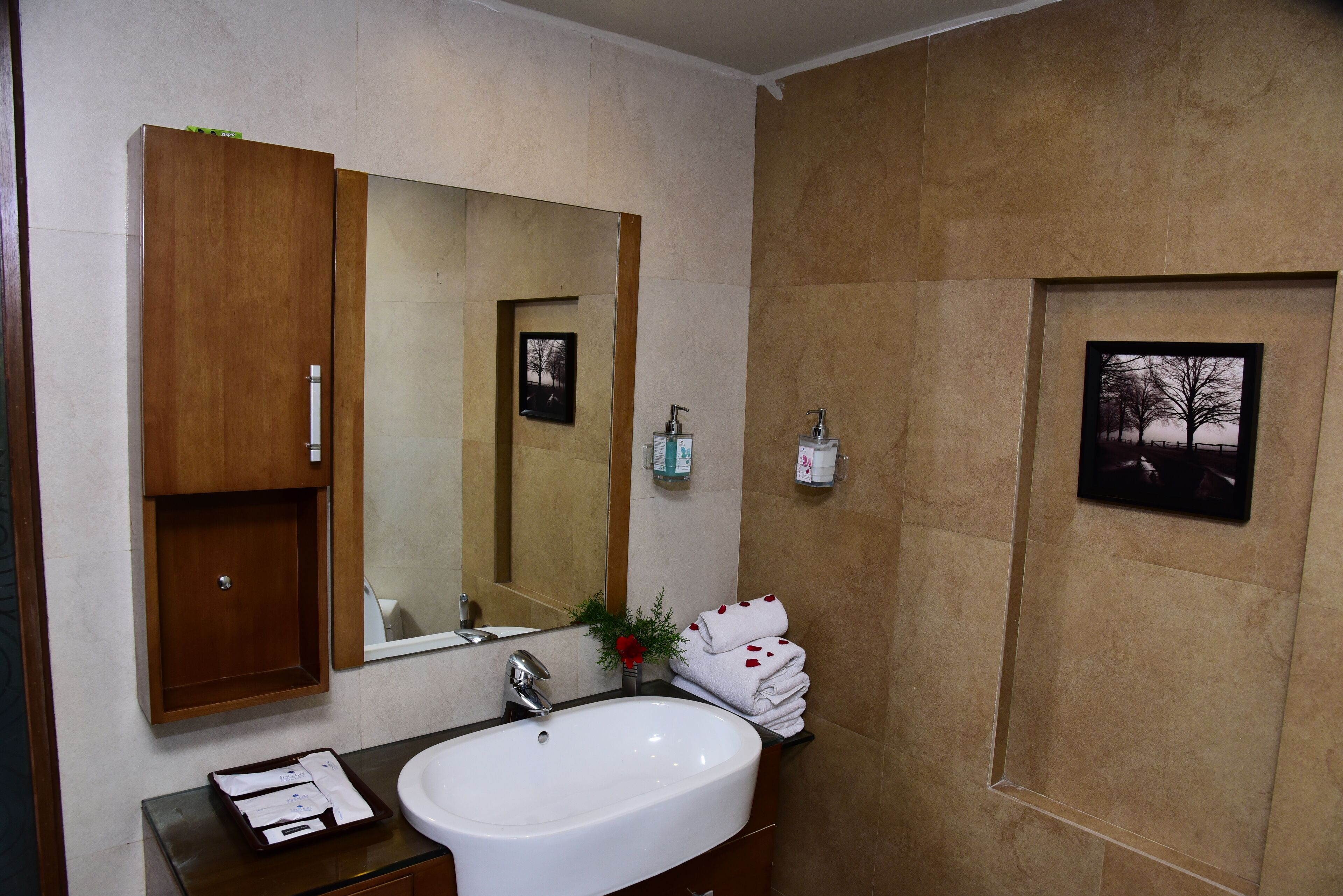 A bathroom with a wooden cabinet, a large mirror, a white sink, and a framed picture on the wall.