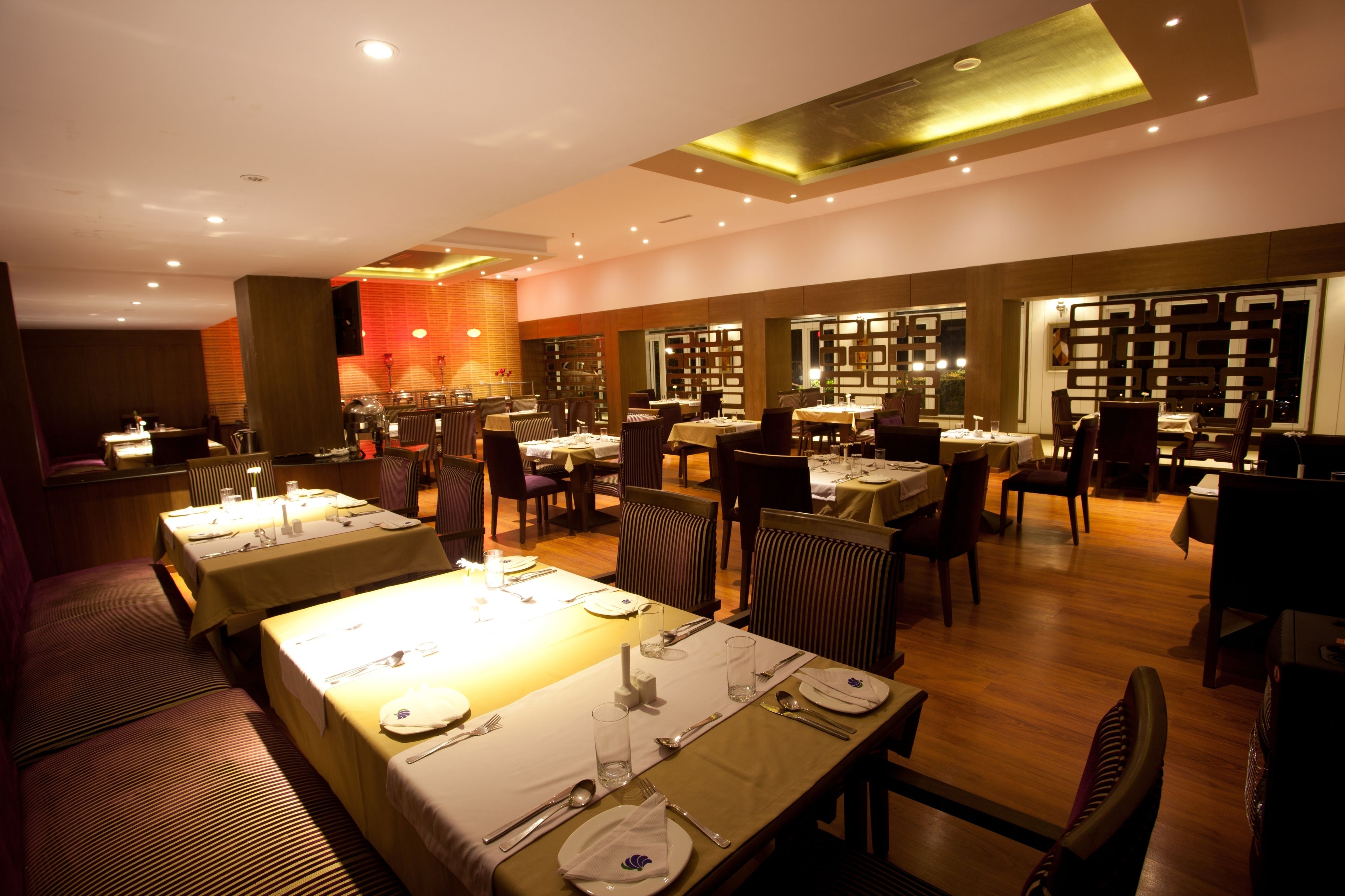A restaurant with multiple dining tables set for guests, featuring a warm ambiance with soft lighting and a modern interior design.