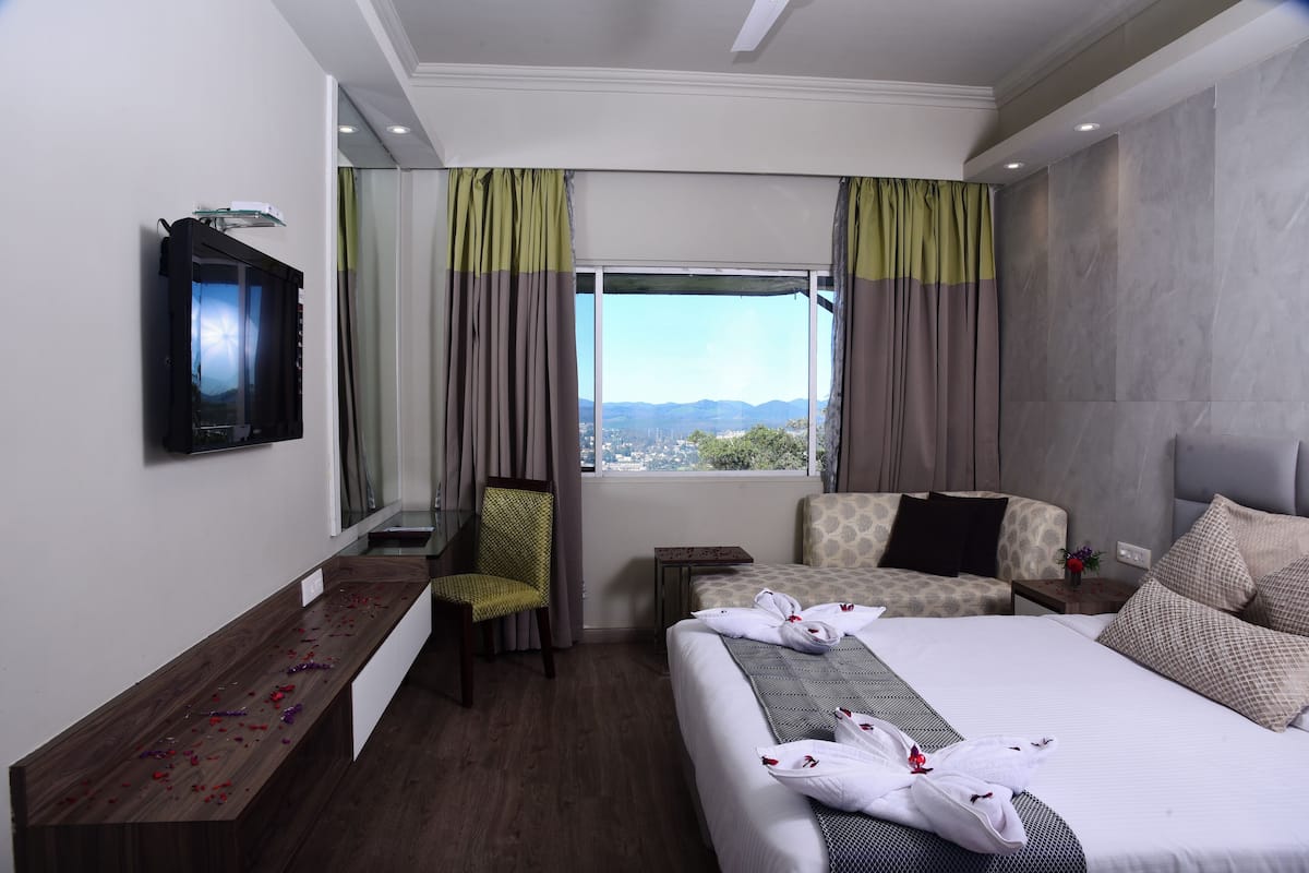 Habitación de hotel con cama, escritorio, silla, televisor y ventana con cortinas.
