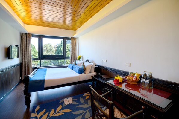 Una habitación de hotel con una cama, un escritorio con una cesta de fruta, dos botellas y un televisor en la pared.