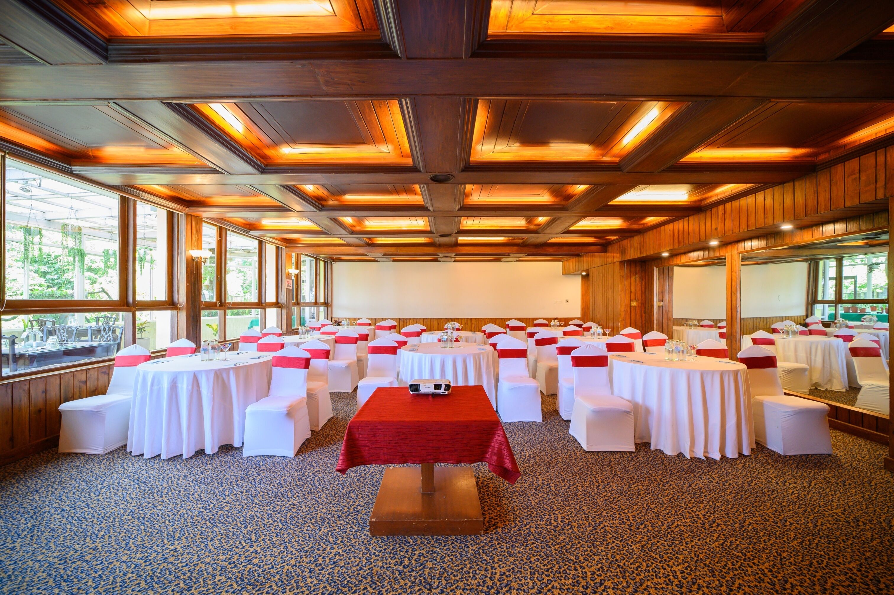A conference room with round tables, white chairs, and red sashes.