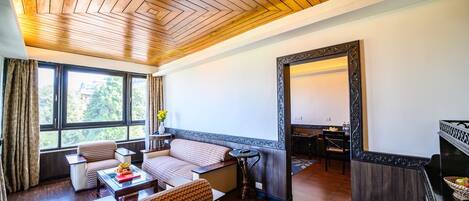 A spacious living room with a wooden ceiling, large windows, a sofa set, a coffee table, and a fireplace.