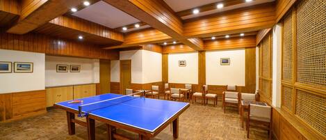 A room with a ping pong table, wooden paneling, and several chairs.