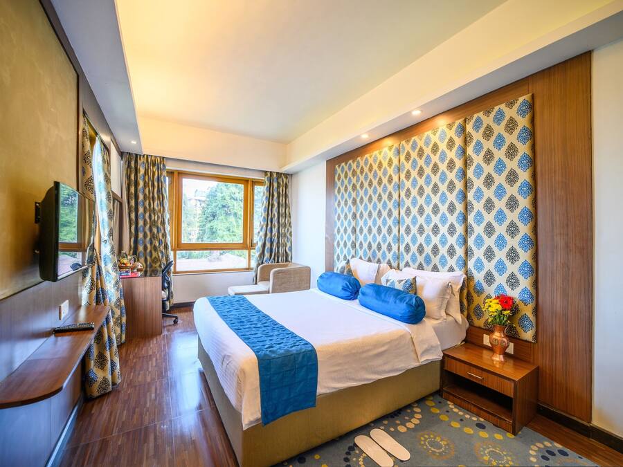 A modern hotel room with a large bed, a TV, a desk, and a window with curtains.