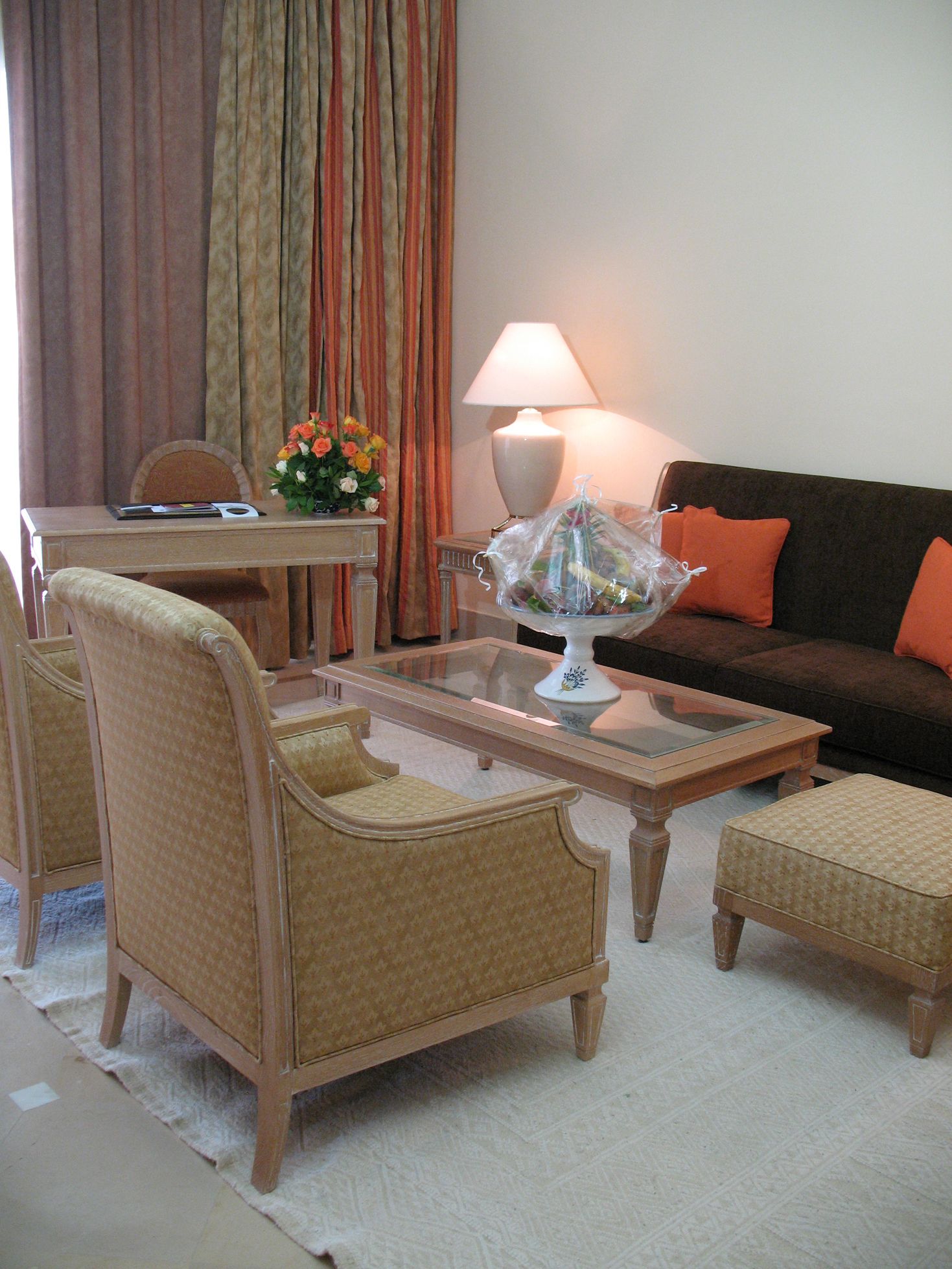 Una sala de estar con sofá, sillones, una mesa de centro, una lámpara y un arreglo floral.
