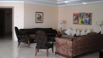 A living room with a sofa, armchairs, and a coffee table. There are wall-mounted lamps and a framed picture on the wall.