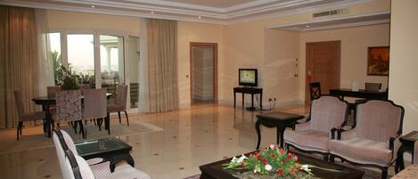 A spacious living room with a glass door leading to a balcony, a television, and a coffee table with flowers.