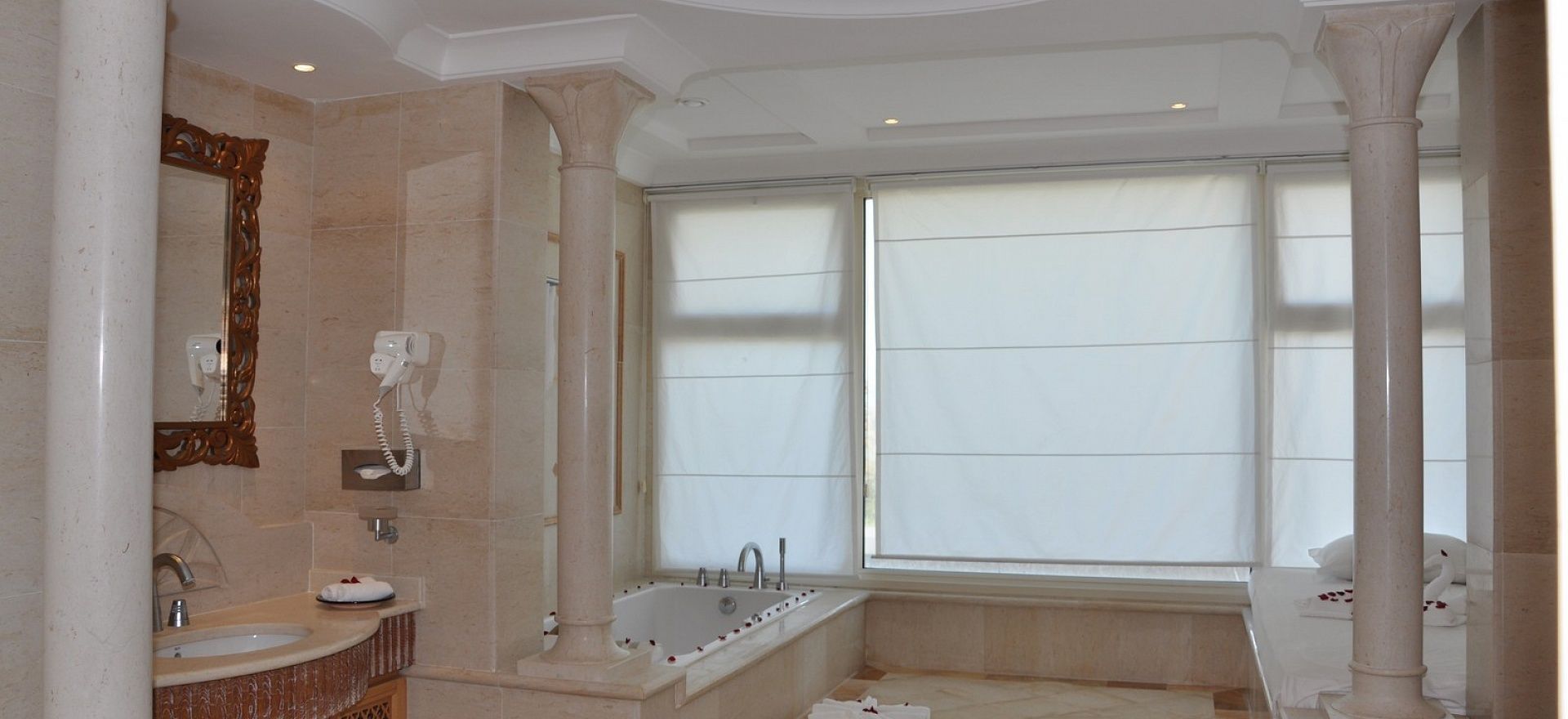 Une salle de bain spacieuse avec une grande baignoire, un meuble-lavabo avec un miroir et une fenêtre laissant entrer la lumière naturelle.