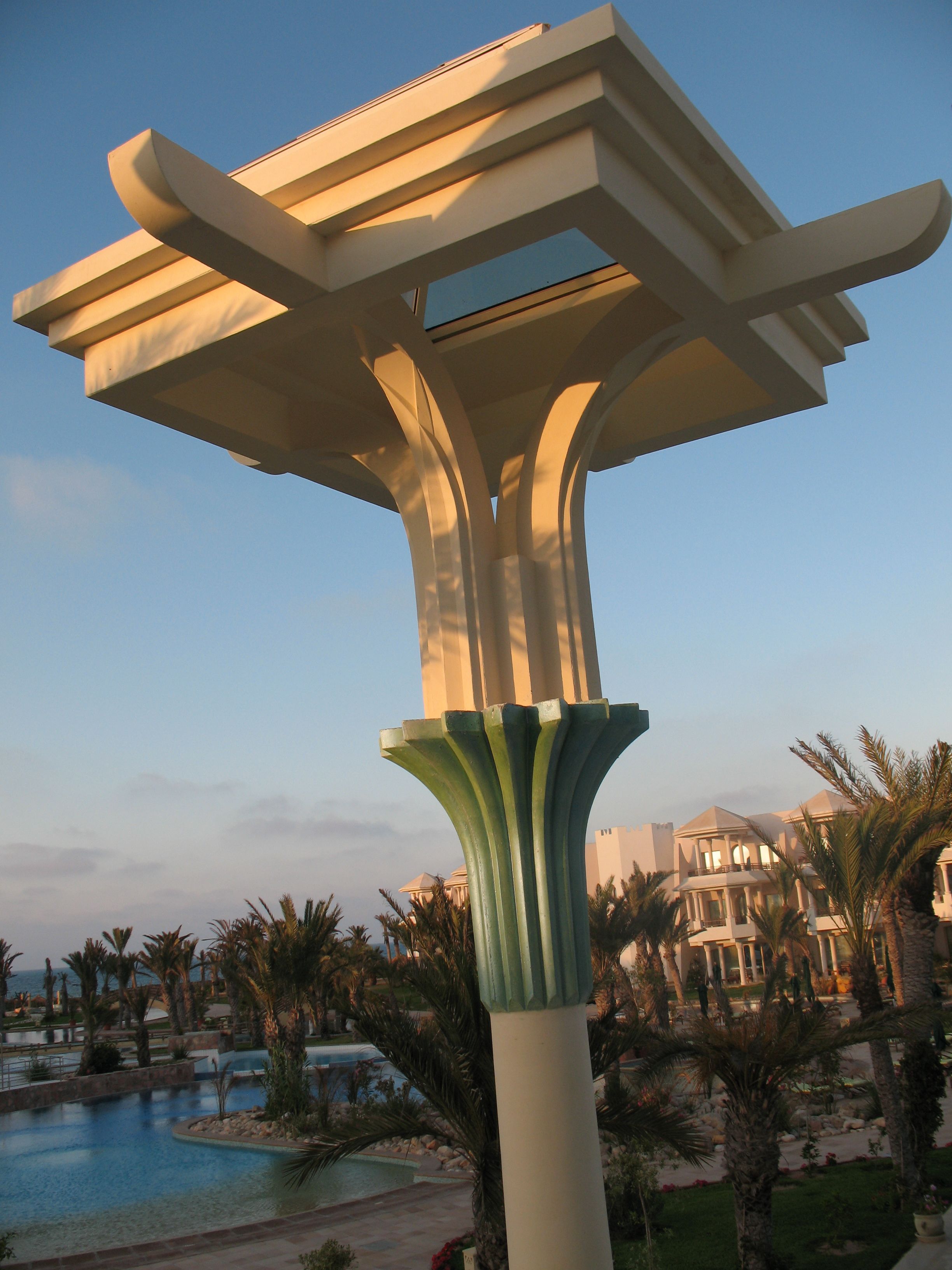 A modern architectural structure with a unique design, surrounded by a pool and palm trees.