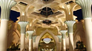 A spacious lobby with high ceilings and large columns, featuring a central chandelier and reflective flooring.