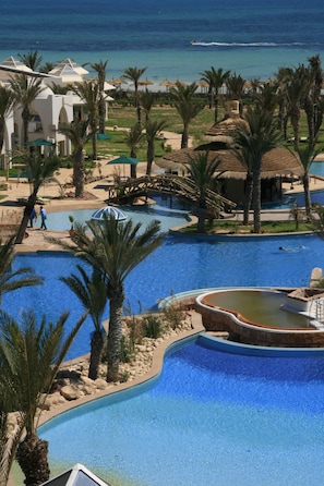 A resort pool area with palm trees, a bridge, and a view of the ocean.
