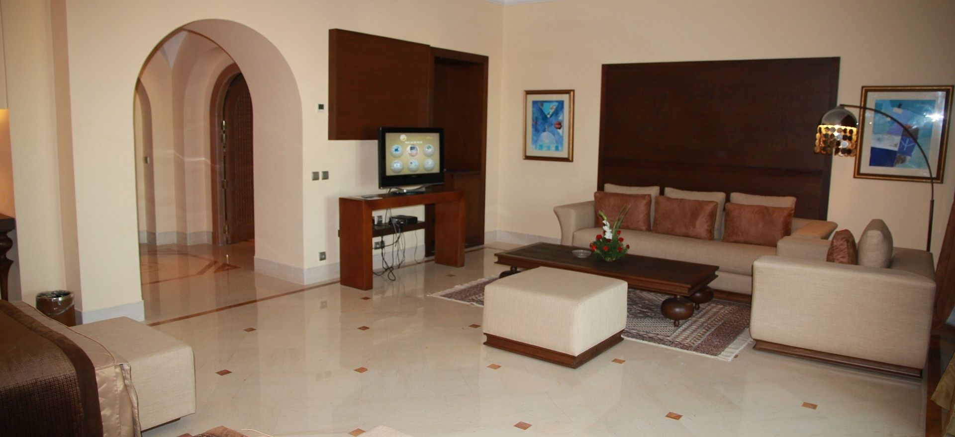 A living room with a sofa, ottoman, coffee table, TV, and artwork on the walls.