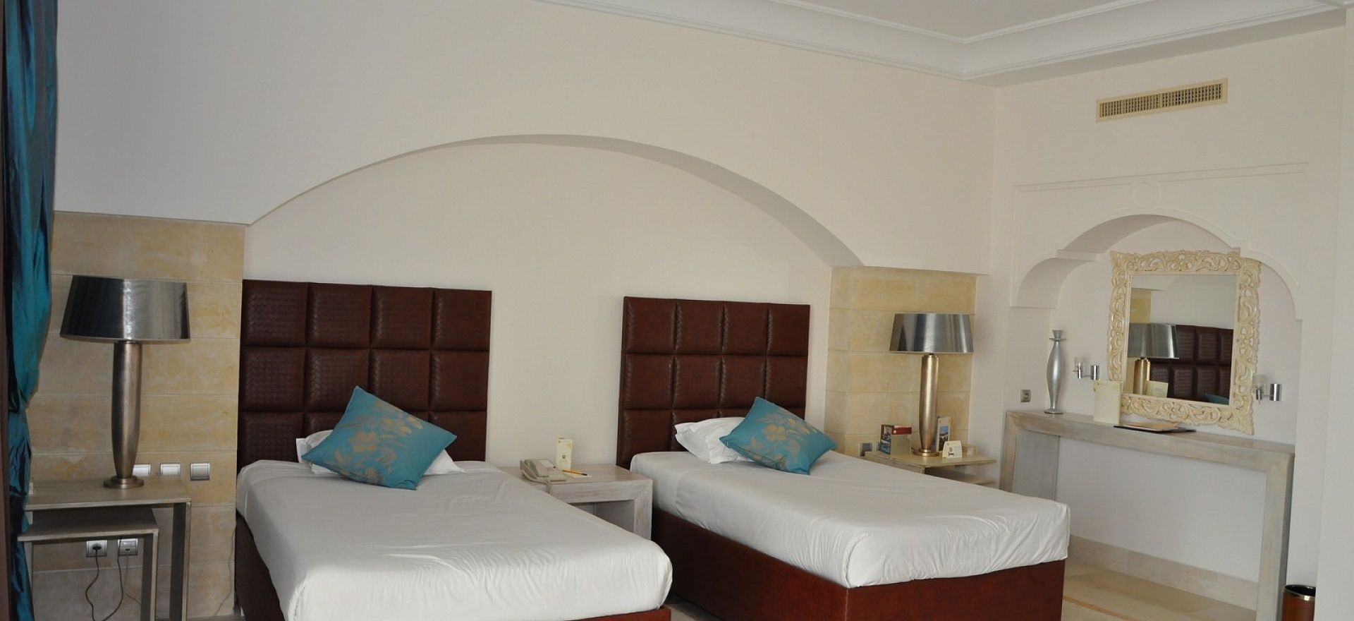 Una habitación de hotel con dos camas, un tocador con espejo y una mesita de noche con lámpara.