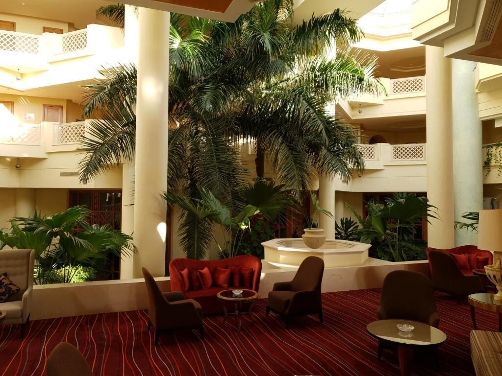 A spacious lobby with a central fountain, multiple seating areas, and lush indoor plants.