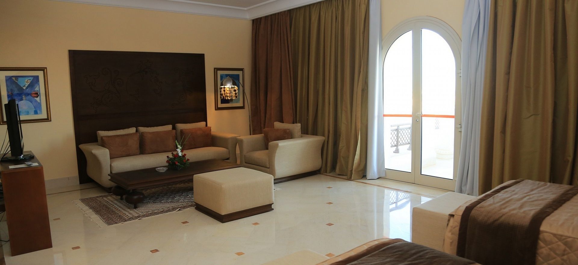 A spacious living room with a large sofa, a coffee table, and a television. There is a large window with curtains and a view of the outside.