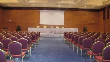 Ein Konferenzraum mit Reihen violetter Stühle und einer Bühne mit weißem Hintergrund.