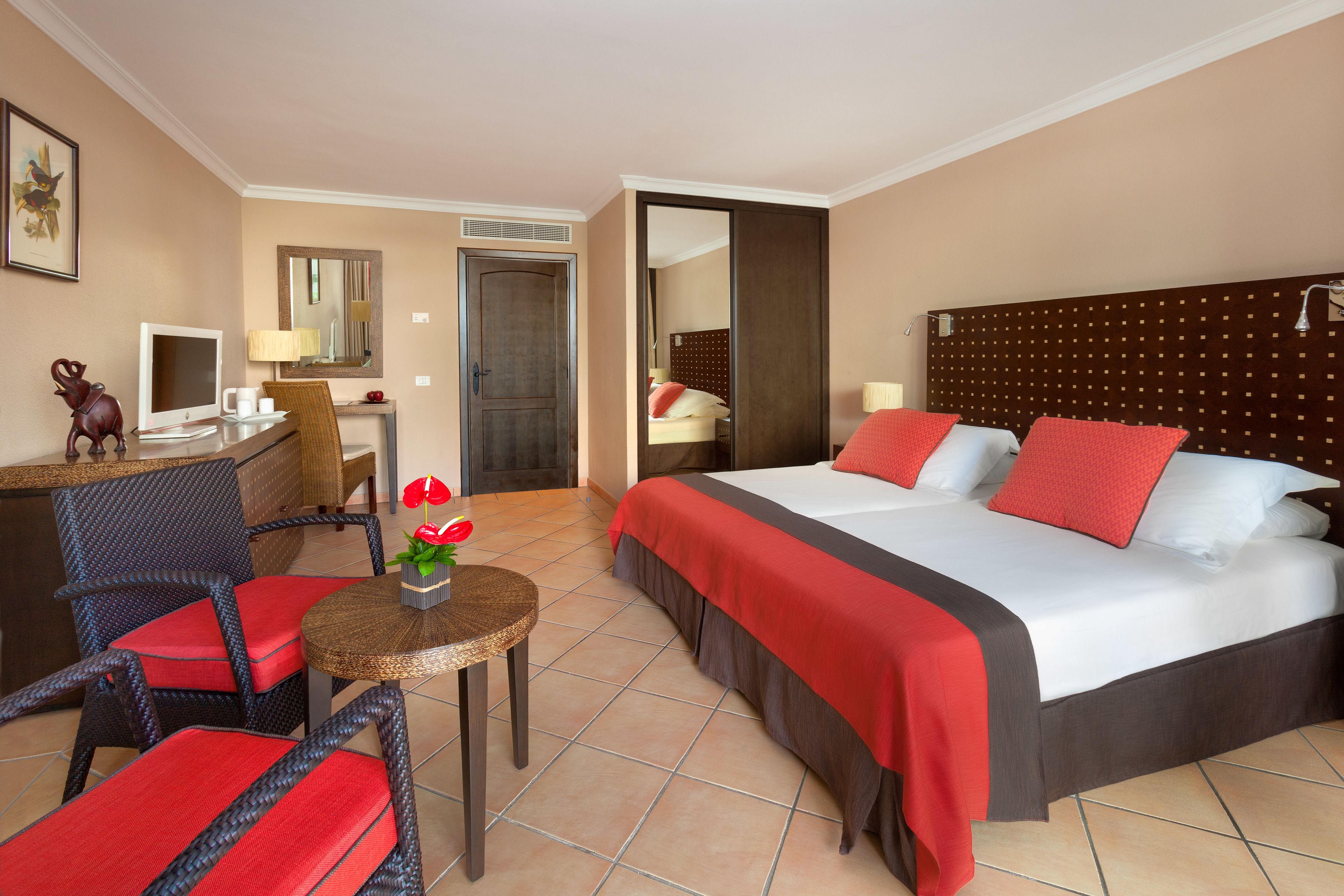 Habitación de hotel con una cama, un escritorio con computadora, una silla y una mesita con flores.