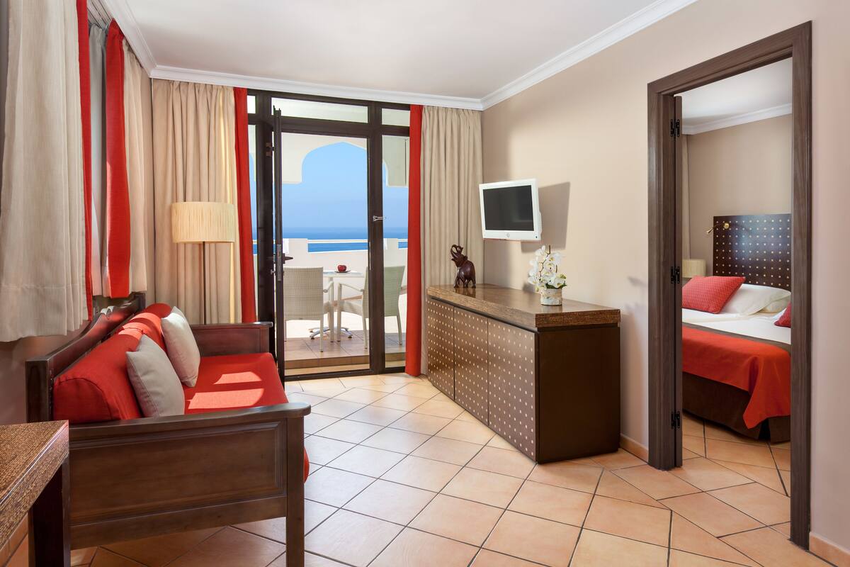 Une chambre d’hôtel avec un balcon, un lit, un canapé, une télévision et un bureau.