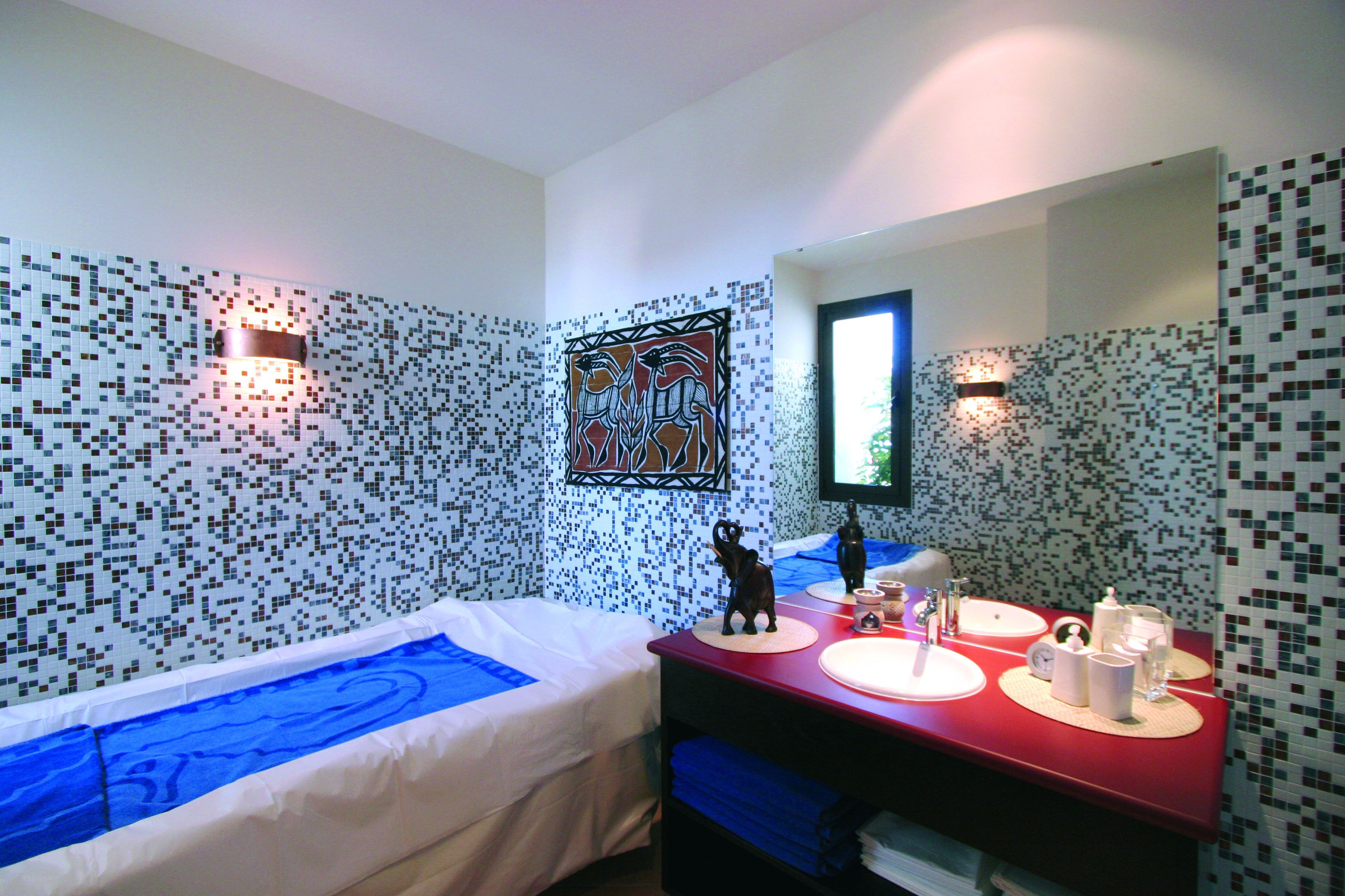 Ein Hotelzimmer mit einem Bett, einem roten Schminktisch mit Spiegel und einer Wand mit Mosaikfliesen.
