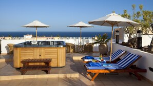 Tagterrasse med jacuzzi, liggestole, parasoller og havudsigt.