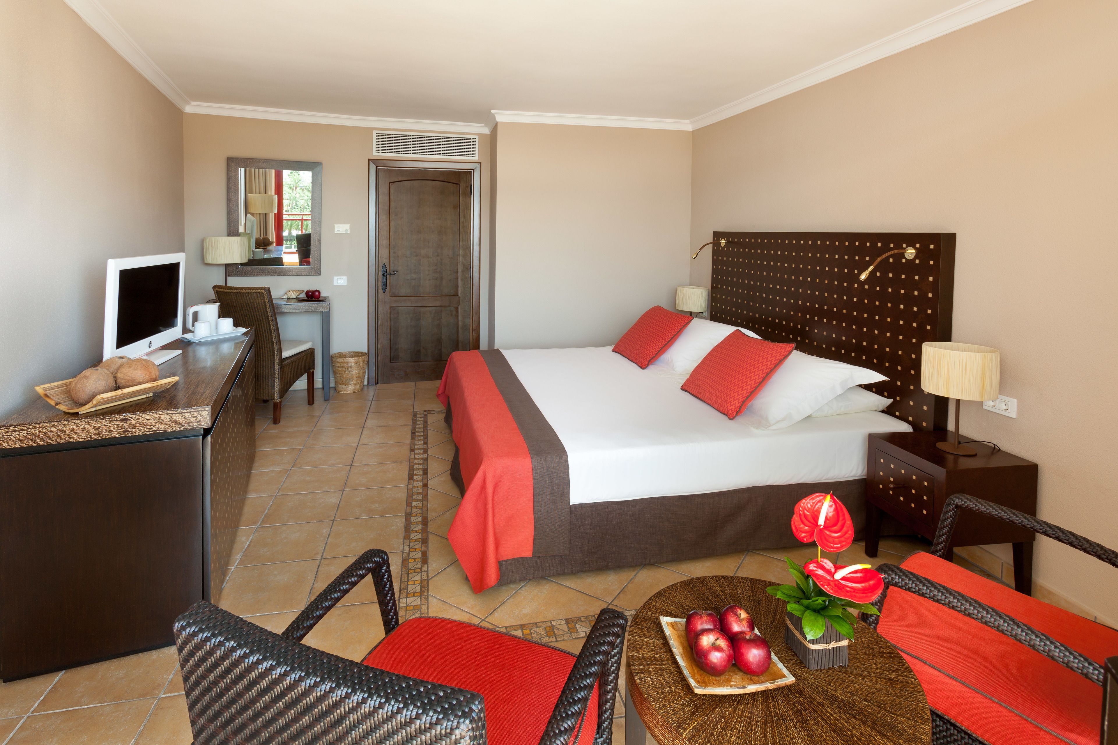 Habitación de hotel con cama, escritorio, silla y una pequeña mesa con manzanas y flores.