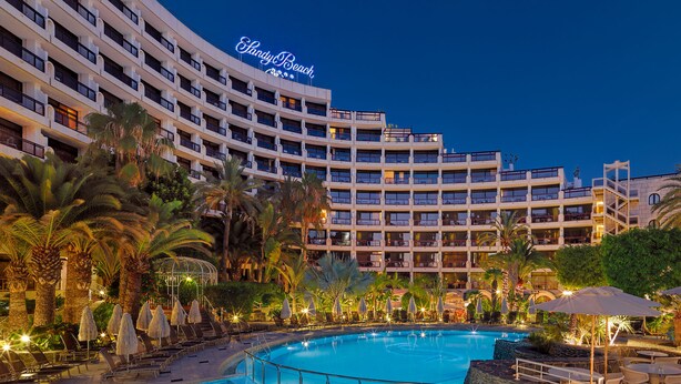 Et hotel med en stor swimmingpool, palmer og et skilt med teksten "Shady Beach".
