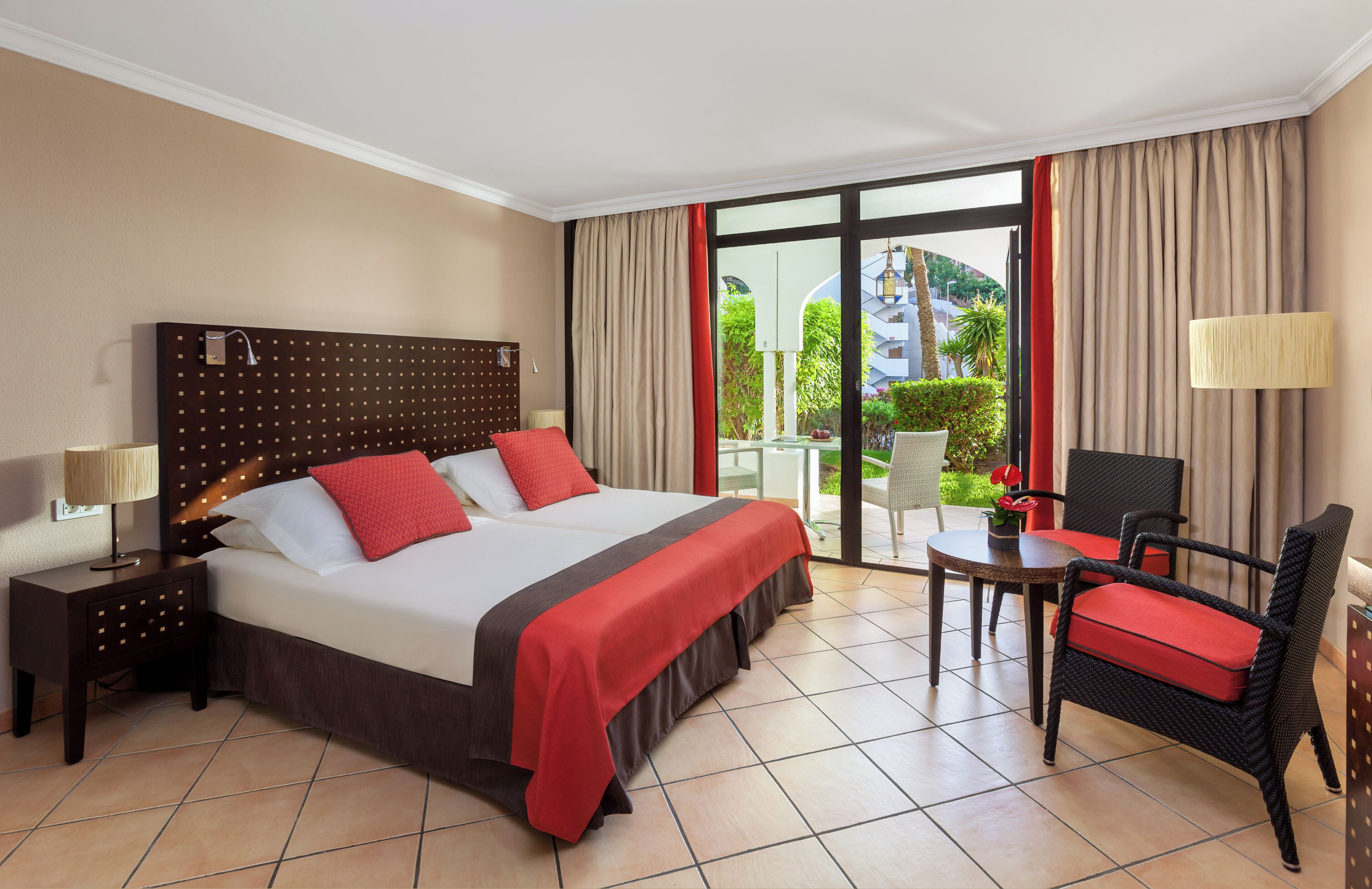 Habitación de hotel con una cama grande, un escritorio, una silla y un balcón con vistas a zonas verdes.