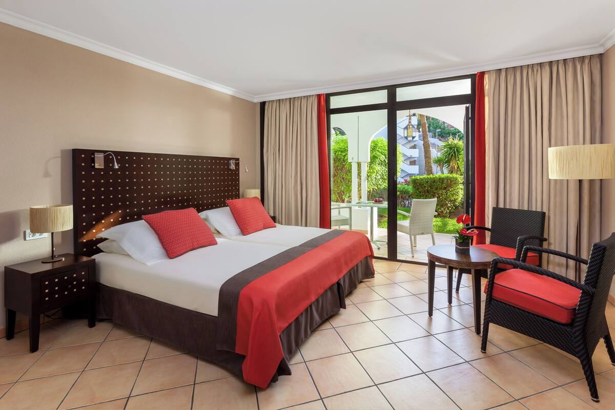 Habitación de hotel con una cama grande, un escritorio, una silla y un balcón con vistas a zonas verdes.
