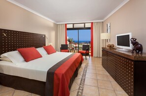 A hotel room with a large bed, a desk with a TV, and a balcony with a view of the ocean. - Seaside Sandy Beach (San Bartolomé de Tirajana)
