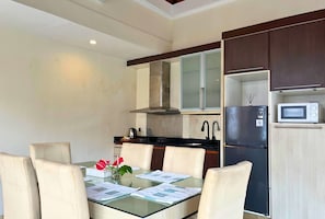 A modern kitchen with a glass dining table, white chairs, a refrigerator, a microwave, and a stove.