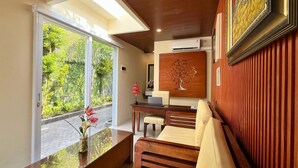 Une pièce avec un plafond en bois, un bureau avec une chaise, un canapé, une grande fenêtre donnant sur un paysage verdoyant et un climatiseur fixé au mur.