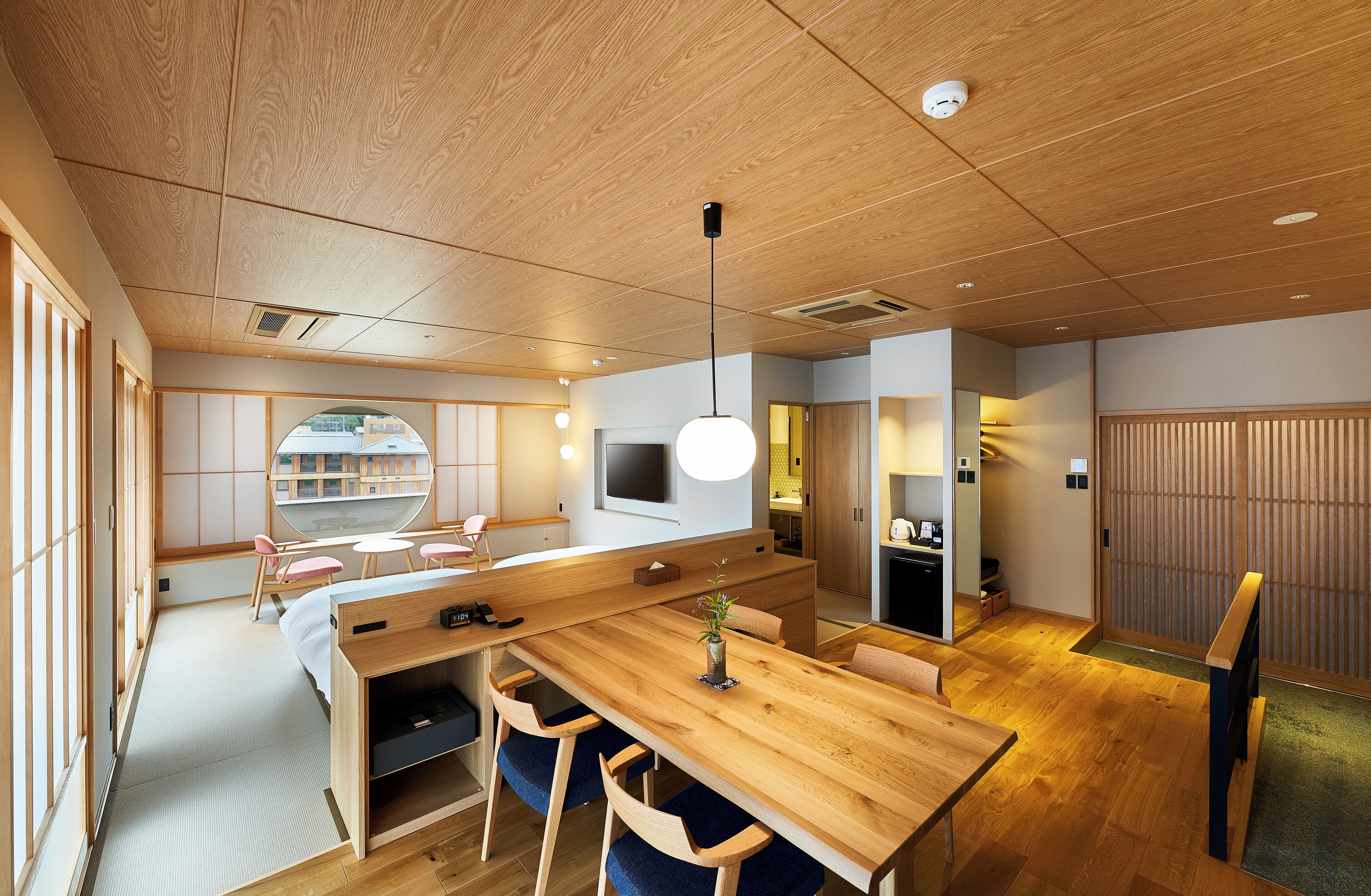 A modern Japanese-style room with a wooden dining table, chairs, a TV, and a tatami mat area.