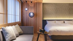 A hotel room with a bed, a sofa, a small table, and two wall-mounted lamps.