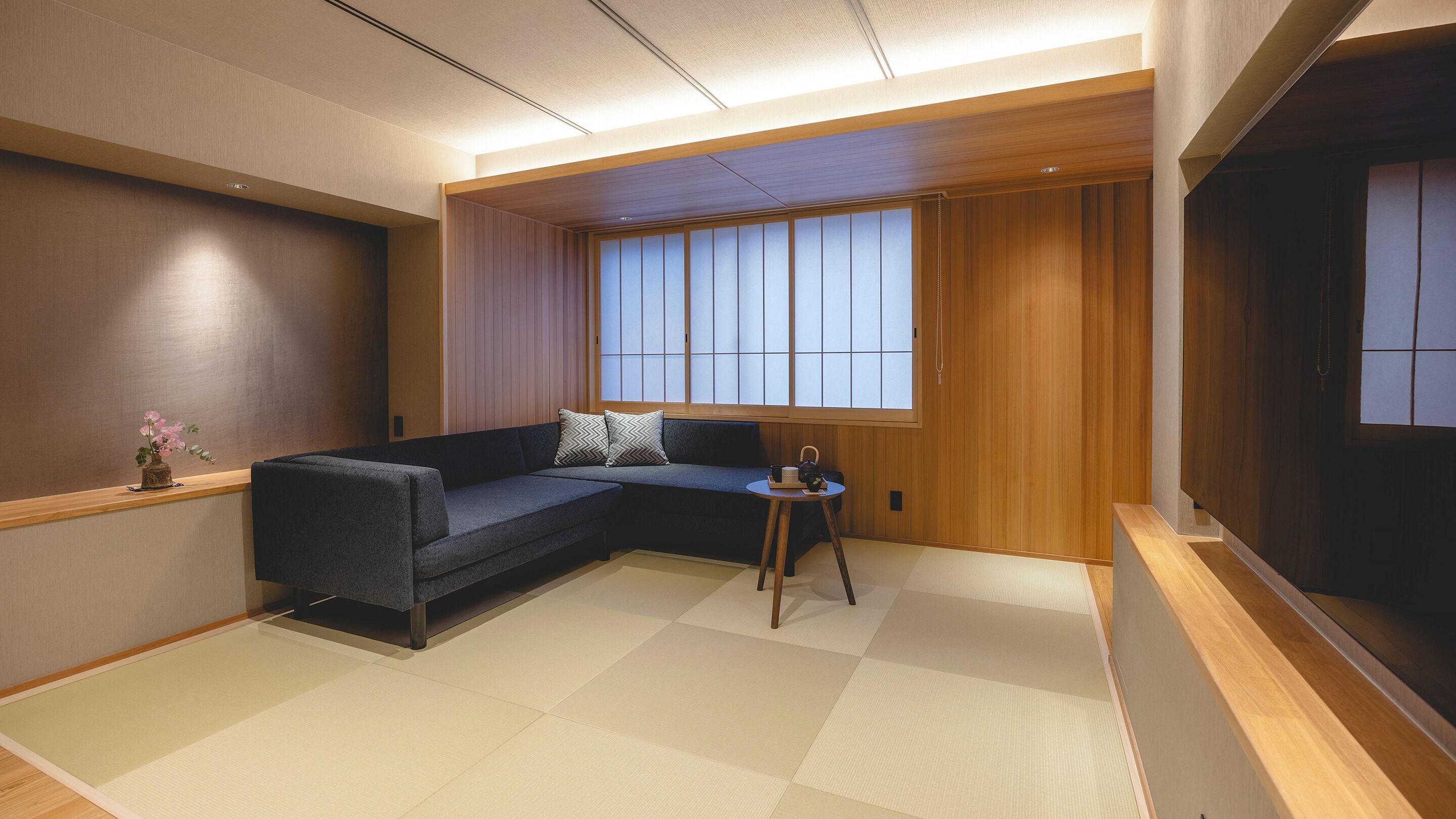 A modern living room with a dark grey sofa, a small wooden side table, and a tatami mat floor.