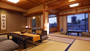 A traditional Japanese room with tatami flooring, a low table with cushions, and a view of a pagoda through large windows. - Asukasou (Nara)