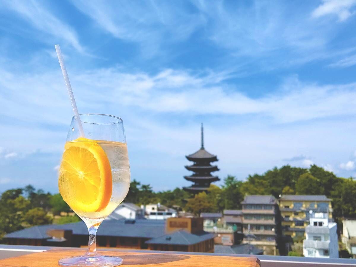 A glass of water with an orange slice on a table with a view of a pagoda in the background.