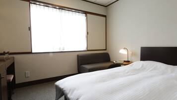 Habitación de hotel con cama, escritorio, silla, lámpara y ventana con persianas.