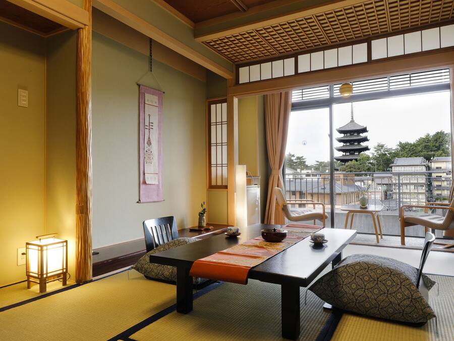 Una habitación japonesa tradicional con suelo de tatami, una mesa baja y vistas a una pagoda a través de amplios ventanales.