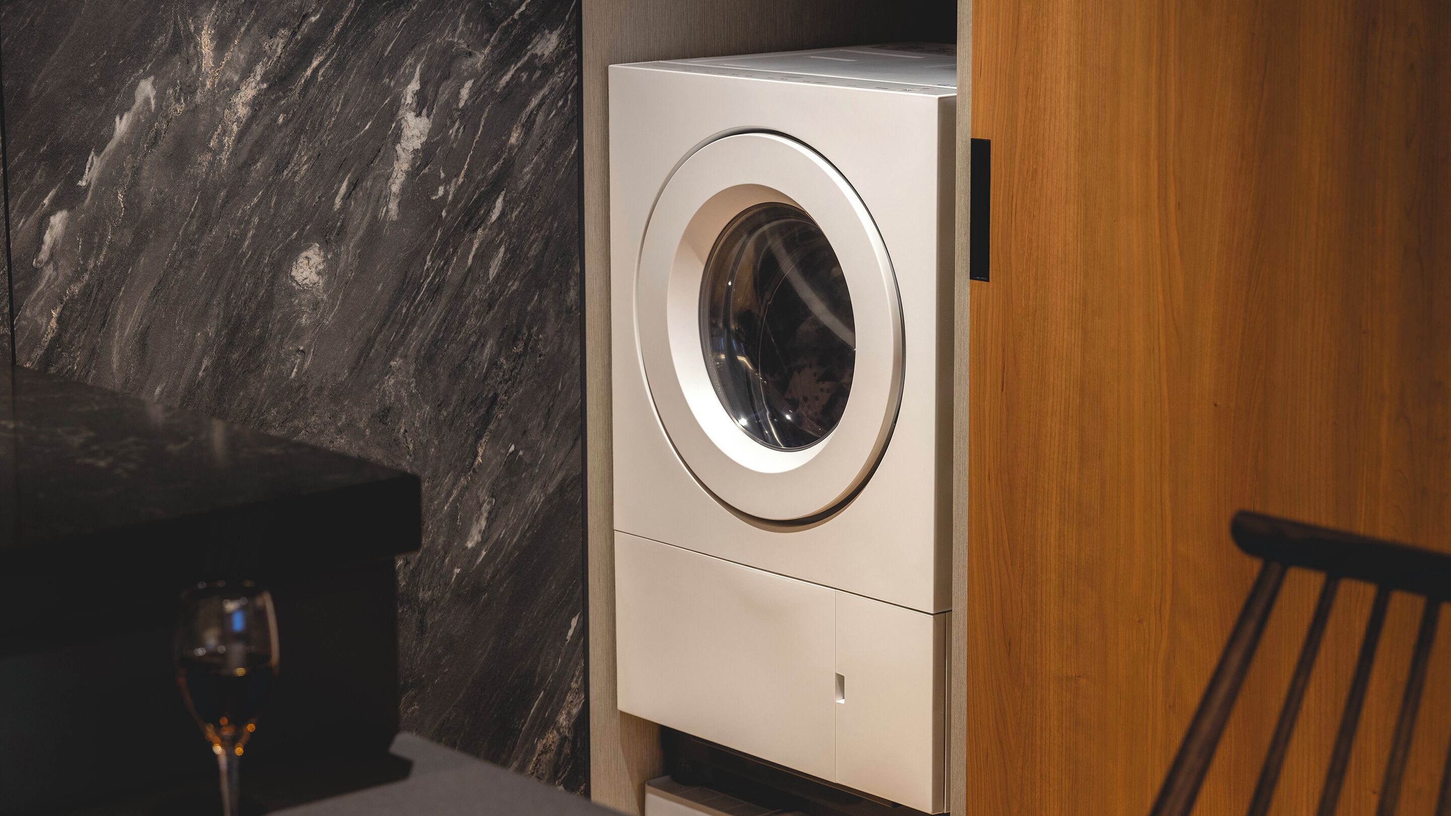 Una lavadora compacta y moderna en un baño elegante y minimalista con una pared de mármol y un mueble de madera.