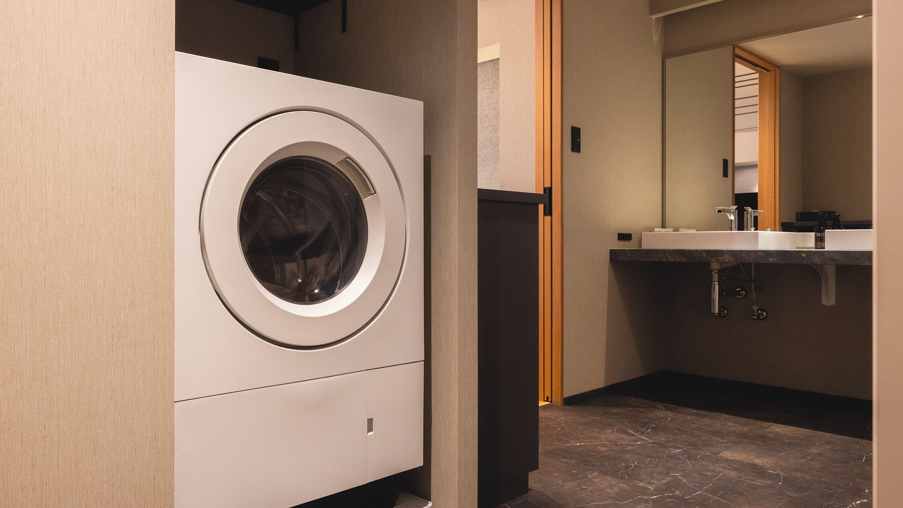 A compact laundry room with a front-loading washing machine, a small countertop with a sink, and a mirror above the sink.