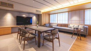 A modern living room with a flat-screen TV, a dining table with chairs, a sofa, and a small side table.