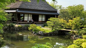 A traditional Japanese-style building with a thatched roof, surrounded by a pond and lush greenery. - Asukasou (Nara)