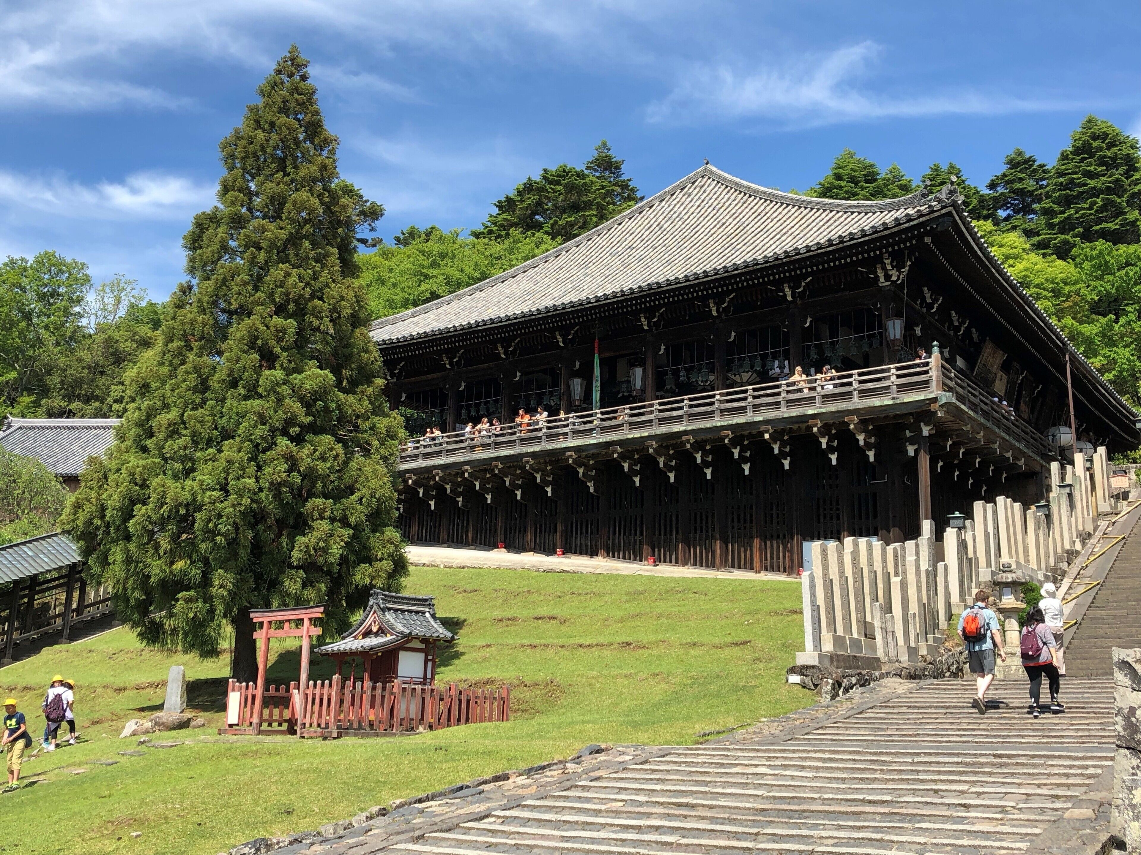 A traditional wooden building with a balcony, surrounded by trees and a stone pathway.