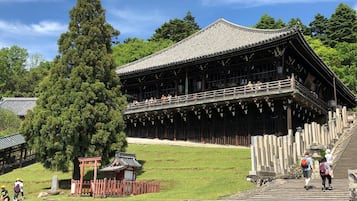 A traditional wooden building with a balcony, surrounded by trees and a stone pathway.