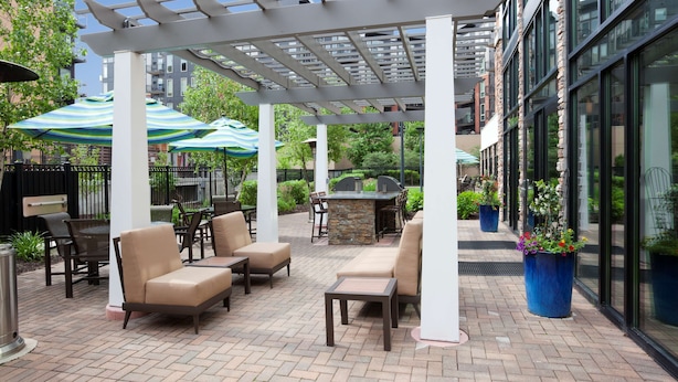 Un espacio al aire libre con patio, mobiliario, sombrillas y una parrilla.