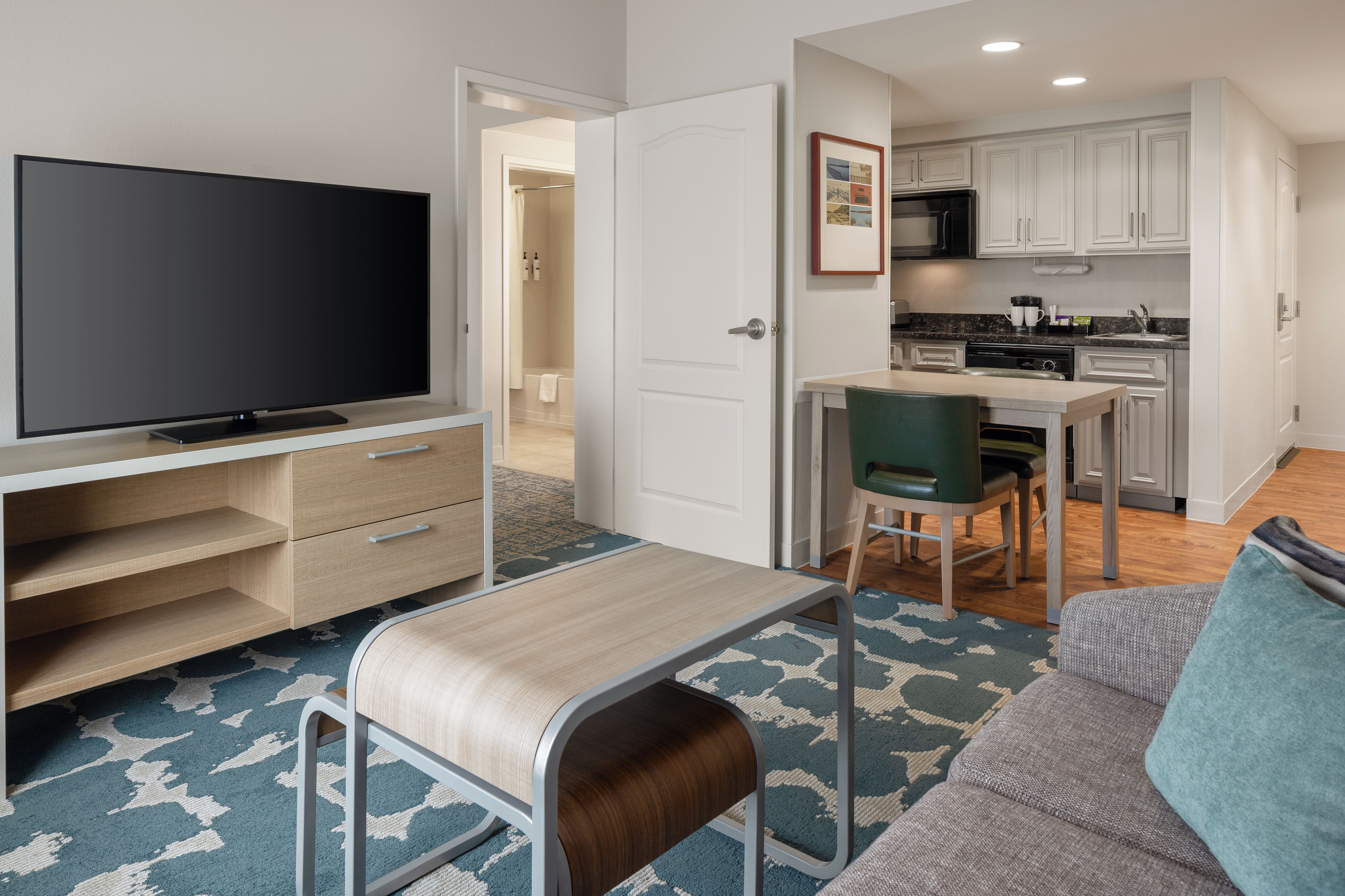 A modern living room with a flat-screen TV, a sofa, a coffee table, and a dining area with a chair and a small table.